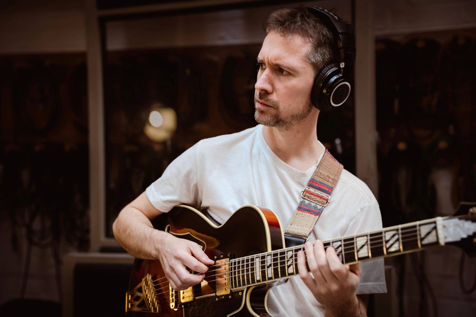 Craig Carri playing an archtop guitar in the studio, wearing headphones